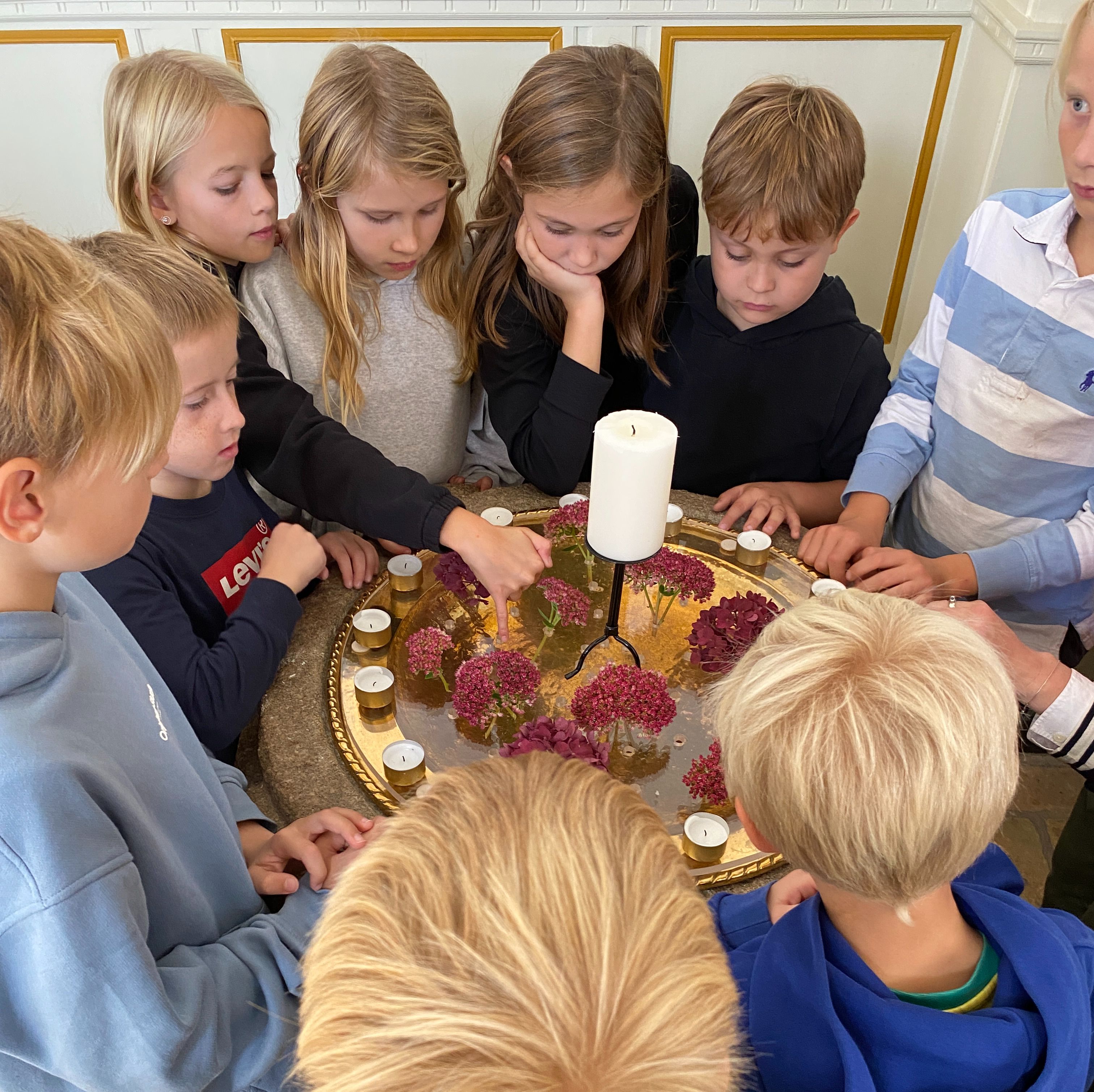Børn står rundt om døbefont med lys på.